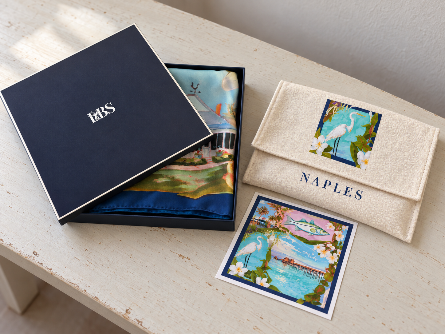 Naples scarf in its navy LBS box beside the cream pouch and art print on a tabletop
